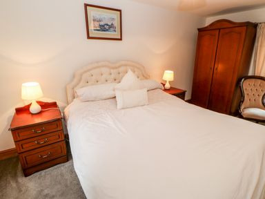 A bedroom with a bed flanked by two nightstands with lamps a wooden wardrobe and a chair at The Hayloft in Milton near Brampton