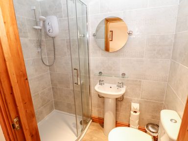 A bathroom with a shower, a round mirror, a pedestal sink, a toilet, and stacked toilet paper at The Hayloft in Milton near Brampton