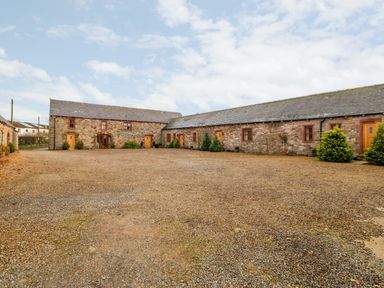 A gravel courtyard surrounded by stone buildings with wooden doors and small windows at The Hayloft in Milton near Brampton