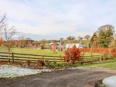 A rural landscape with a gravel driveway, wooden fences, trees with autumn leaves and buildings in the distance at The Hayloft in Milton near Brampton