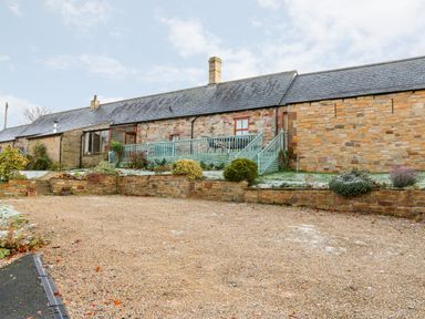 A stone house with a gravel driveway and a garden with shrubs and a blue railing at The Hayloft in Milton near Brampton