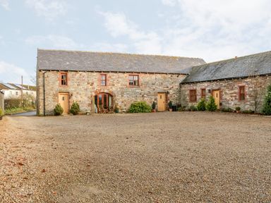 An exterior view of a stone building with wooden doors and windows and a gravel courtyard at The Hayloft in Milton near Brampton