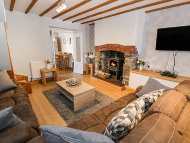 A living room with brown sofas a wooden coffee table a fireplace with fire a wall mounted tv and wooden beams on the ceiling at Tryfan in Llanberis