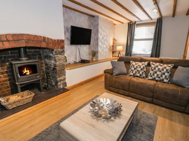 A living room with a brown sofa and checkered pillows a wooden coffee table and a fireplace with a wood stove at Tryfan in Llanberis