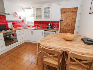 A kitchen with wooden table and chairs red tiled backsplash and wooden door at Tryfan in Llanberis