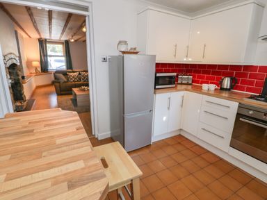 A kitchen with white cabinets red tile backsplash wooden countertops and a small dining table with a stool at Tryfan in Llanberis