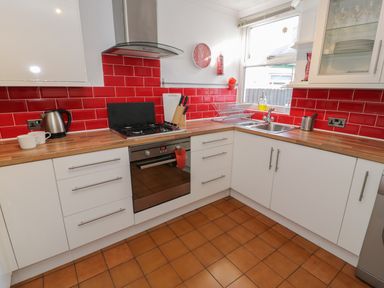 A kitchen with white cabinets red tile backsplash a stove kettle and sink at Tryfan in Llanberis
