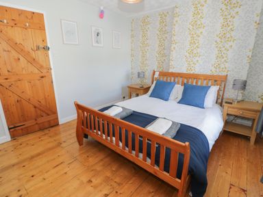 A bedroom with a wooden bed frame blue pillows and wooden bedside tables at Tryfan in Llanberis