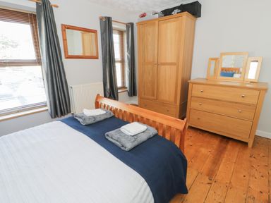 A bedroom with a wooden bed a chest of drawers with a mirror a wooden wardrobe and two windows with curtains at Tryfan in Llanberis