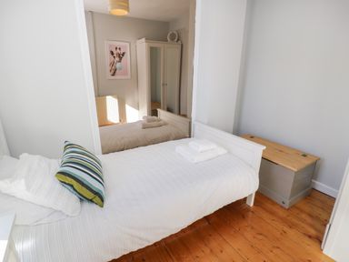 A bedroom with a white bed, striped pillow, folded towels on the bed, a mirrored wardrobe, a wooden chest, and a giraffe picture on the wall at Tryfan in Llanberis
