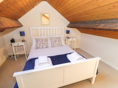 A bedroom with a white bed frame, floral pillows, blue lamps on bedside tables, and wooden slanted ceiling at Tryfan Llanberis
