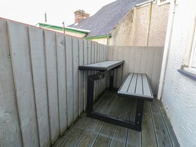 An outdoor corner with a wooden picnic table and bench on a deck surrounded by wooden fencing