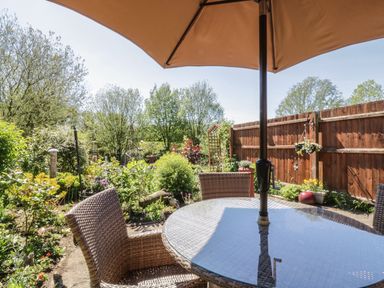 A garden patio with a glass table and wicker chairs under a large umbrella at Kingfisher in Wattisfield near Rickinghall and Diss