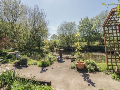 A garden with potted plants a birdbath wooden trellis and a pond surrounded by trees at Kingfisher in Wattisfield near Rickinghall and Diss