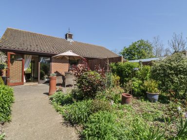 A garden with potted plants and a patio area outside a single-story brick house at Kingfisher in Wattisfield near Rickinghall and Diss