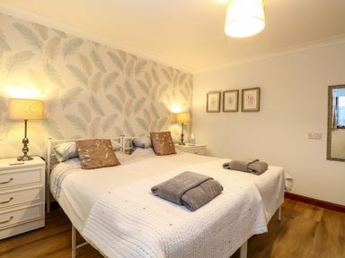 A bedroom with a double bed two bedside tables and lamps wooden floor and framed pictures on the wall at Kingfisher in Wattisfield near Rickinghall and Diss