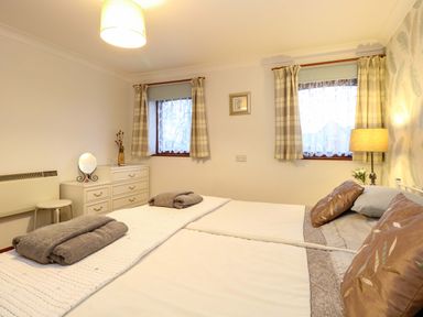 A bedroom with a double bed two windows with curtains a dresser with a mirror and a lamp at Kingfisher Wattisfield near Rickinghall and Diss