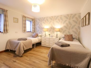 A bedroom with two single beds bedside table with lamps and a wallpapered accent wall at Kingfisher in Wattisfield near Rickinghall and Diss