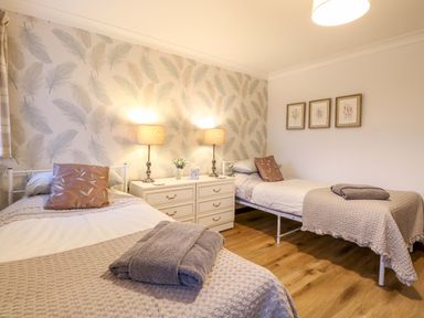 A bedroom with two single beds a chest of drawers with lamps and framed pictures on the wall at Kingfisher Wattisfield near Rickinghall and Diss