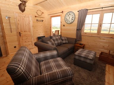 A small living room with plaid upholstered armchairs a gray sofa ottoman wooden walls and a window at The Shooting Lodge in Longnor