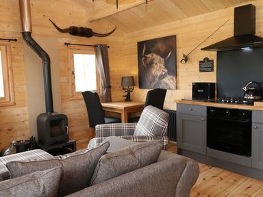 A living area with a wood stove a dining table with chairs a kitchen with an oven kettle and bread box and seating at The Shooting Lodge in Longnor