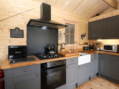 A kitchen with grey cabinets wooden countertops a gas stove oven a white farmhouse sink and a microwave at The Shooting Lodge in Longnor