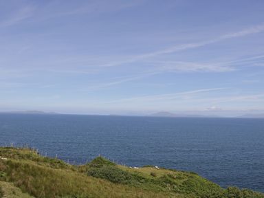 Cliffside grassy area overlooking a large body of water under a blue sky with some clouds