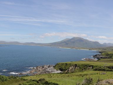 A coastal landscape with rocky shoreline and green hills beside a large body of water at Seaspray in Tully County Galway