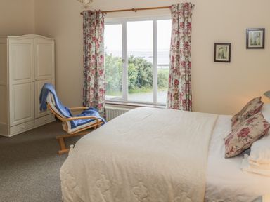 A bedroom with a bed with floral pillows a wooden chair with a blue blanket a white wardrobe and floral curtains on the window at Seaspray in Tully County Galway