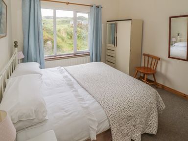 A bedroom with a bed near a window blue curtains a wardrobe a wooden chair and a wall mirror at Seaspray in Tully County Galway