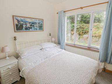 A bedroom with a double bed bedside tables lamps a large window with curtains and a painting on the wall at Seaspray in Tully County Galway