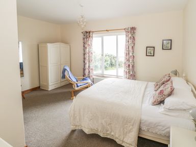 A bedroom with a bed with floral pillows a wardrobe a chair with blue blanket a window with floral curtains and two pictures on the wall at Seaspray in Tully County Galway