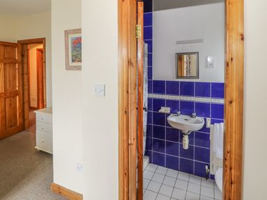 A hallway with wooden doors and a white dresser next to a bathroom with blue tiles and a white sink at Seaspray in Tully County Galway