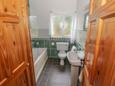 A bathroom with wooden doors a bathtub white toilet white sink and a frosted window at Seaspray in Tully County Galway