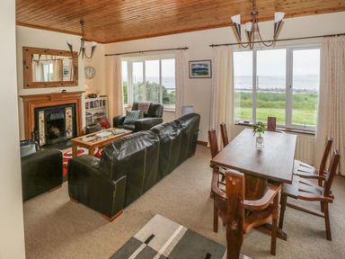 A living room with black leather sofas a wooden dining table with chairs and a fireplace at Seaspray in Tully County Galway