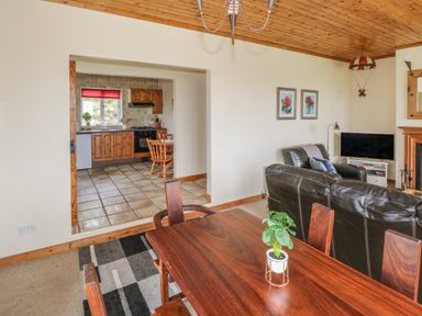 A living room with leather sofas a television and a wooden dining table with a plant at Seaspray in Tully County Galway