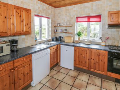 A kitchen with wooden cabinets tiled walls two windows red blinds countertop appliances and a tiled floor at Seaspray in Tully County Galway