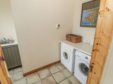 A laundry room with a washing machine, dryer, sink, and a woven basket on the counter at Seaspray in Tully County Galway