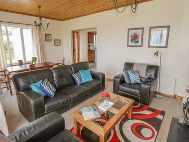 A living room with black leather sofas a wooden coffee table with books and flowers a dining table with chairs and framed artwork on the walls at Seaspray in Tully County Galway
