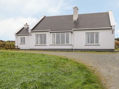 A single story white house with multiple windows a chimney a gravel driveway and grass in front at Seaspray in Tully County Galway