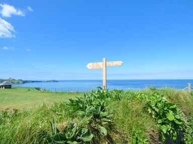A coastal landscape with green vegetation a wooden signpost and the sea in the background at Saltwater One Lusty Glaze Newquay