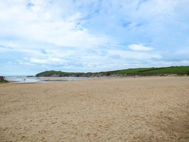 A sandy beach with a few people near the shoreline and green hills in the background at Saltwater One Lusty Glaze in Newquay