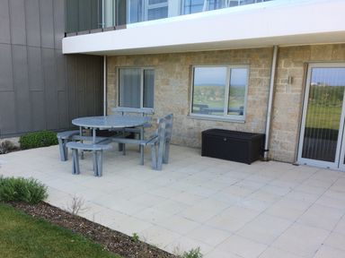 An outdoor patio area with a round table and bench seating next to a building with stone walls and windows at Saltwater One Lusty Glaze Newquay
