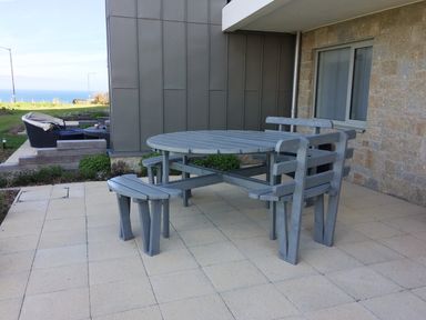 An outdoor patio area with a gray wooden picnic table and benches next to a stone wall at Saltwater One Lusty Glaze in Newquay