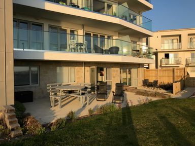 A patio area with outdoor furniture and chairs outside a modern apartment building at Saltwater One Lusty Glaze in Newquay