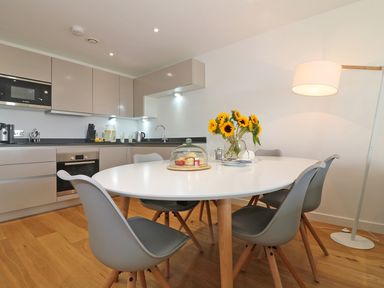 A kitchen and dining area with a white oval table surrounded by gray chairs and sunflowers in a vase at Saltwater One Lusty Glaze in Newquay