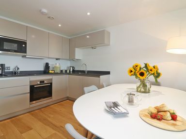 A kitchen with beige cabinets a white dining table with flowers and food at Saltwater One Lusty Glaze in Newquay