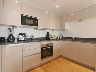 A modern kitchen with beige cabinets black countertop built in oven microwave blender coffee machine and a sink at Saltwater One Lusty Glaze in Newquay