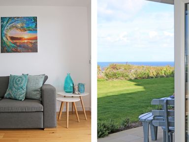 A living room with a grey sofa and blue cushions next to white nested tables with blue glass vases and a view of a garden and ocean at Saltwater One Lusty Glaze in Newquay