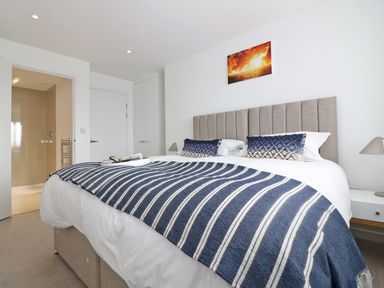 A bedroom with a bed covered by a striped blue and white blanket a bedside table and an open door leading to a bathroom at Saltwater One Lusty Glaze in Newquay